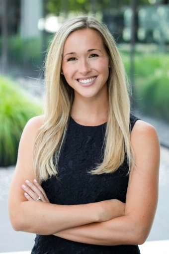 Dr. Wilson portrait, smiling in a black sleeveless dress, arms crossed, outdoor background.